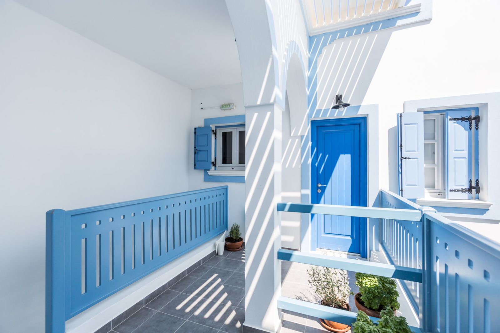 Upper-floor walkway with blue apartment door and herbs in pots